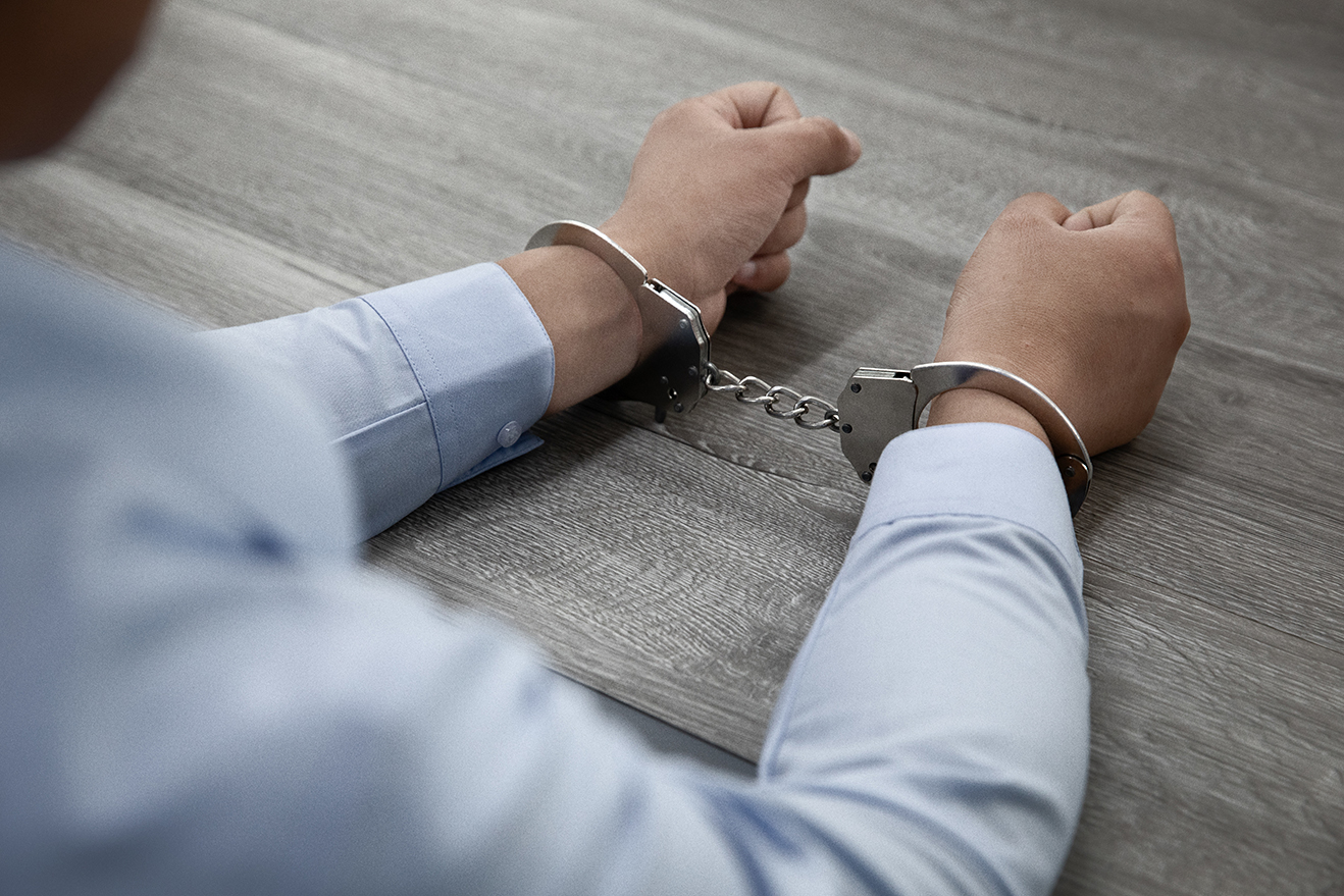 selective-focus-shot-male-hands-handcuffs-wooden-table