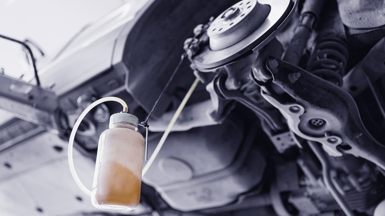 10-a-brake-bleeding-process-on-a-raised-vehicle-showing-a-container-partially-filled-with-old-brake-fluid-connected-by-a-hose-to-the-brake-caliper
