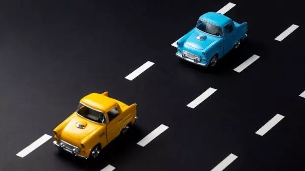 3-toy-yellow-car-and-toy-blue-car-on-a-black-surface-designed-to-look-like-a-two-lane-road-with-white-dashed-lines-620x348