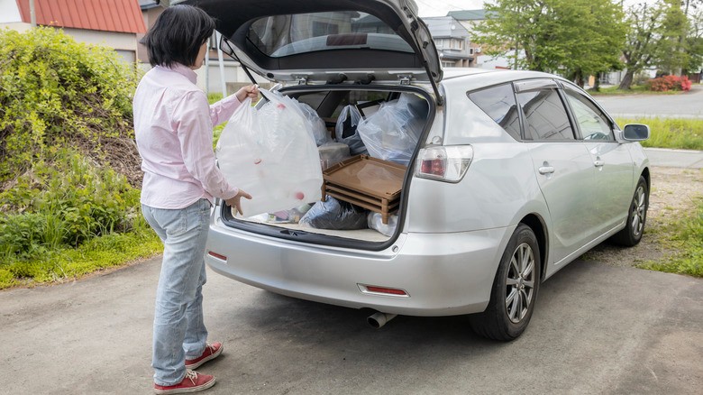 12-a-person-holding-a-large-bag-of-trash-while-looking-at-the-full-trunk-of-a-silver-hatchback