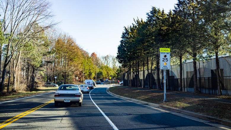 2-cars-driving-on-a-two-lane-road-past-a-school-zone-sign-showing-a-25-mph-speed-limit